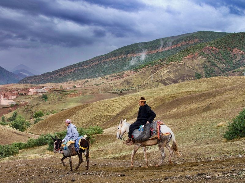 Two men riding down the High Atlas Mountains on their horses or mules to the market