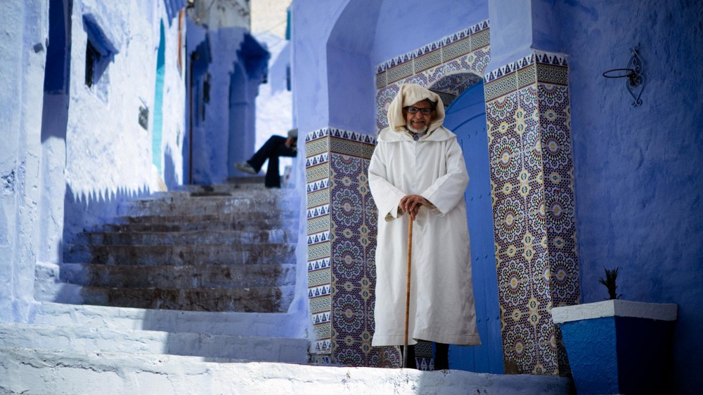 portrait of a man in a white djellaba against the blue walls of Chefchaouen