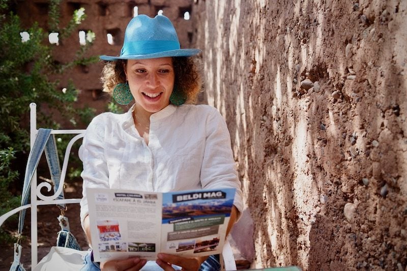 Local Moroccan woman sits down at a cafe in Marrakesh wearing a blue hat reading Beldi Mag