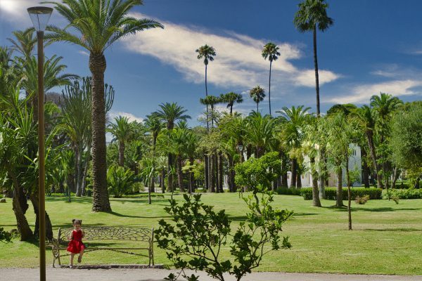 Little girl in red dress sits on a bench near the villa harris museum of tangier in morocco on a sunny day